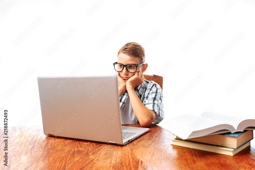 A young man resting after school sitting at the table and watching a movie on a laptop, throwing his hands behind his head, on a white background, in the Studio A young man resting after school sitting at the table and watching a movie on a laptop, throwing his hands behind his head, on a white background, in the Studio