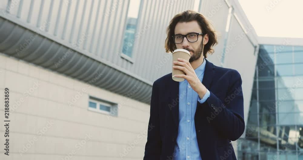 Good looking Caucasian man walking the street and sipping coffee, then taking his smartphone and using it. Good looking Caucasian man walking the street and sipping coffee, then taking his smartphone and using it.