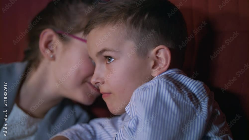 Girl whispering to boy watching movie in cinema. Children exchange impressions about film. Close up of boy watching cinema movie in slow motion. Child movie entertainment Girl whispering to boy watching movie in cinema. Children exchange impressions about film. Close up of boy watching cinema movie in slow motion. Child movie entertainment
