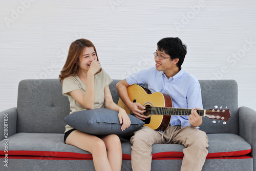 Attractive young Asian couple playing acoustic guitar together in living room. Love and romance people concept.