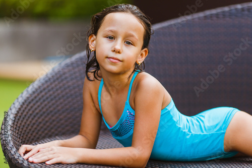 Charming girl 8 years old sunbathing on a wicker sofa in the courtyard of the hotel
