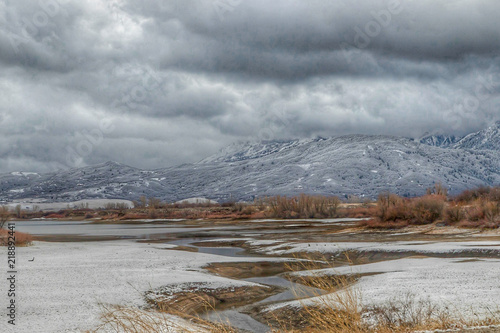 meandering stream flowing into lake in winter with snow and clouds
