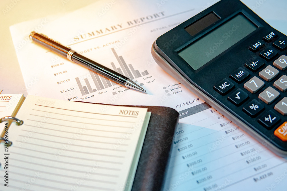 Calculator, pen, blank lined paper page of notebook and summary report paperwork with bar graph and table. Financial data analysis. Business planning and management concept Calculator, pen, blank lined paper page of notebook and summary report paperwork with bar graph and table. Financial data analysis. Business planning and management concept