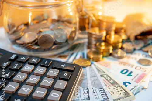 Calculator with currency glass jar and gold coins stack, dollar and euro banknotes on the table. Compound interest rate calculation or financial investment business concepts