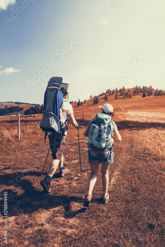 Young couple hike in mountains with baby carrier and backpacks
