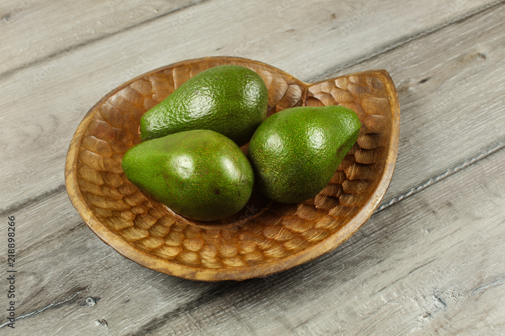 Three whole green avocados on wooden carved bowl. Three whole green avocados on wooden carved bowl.
