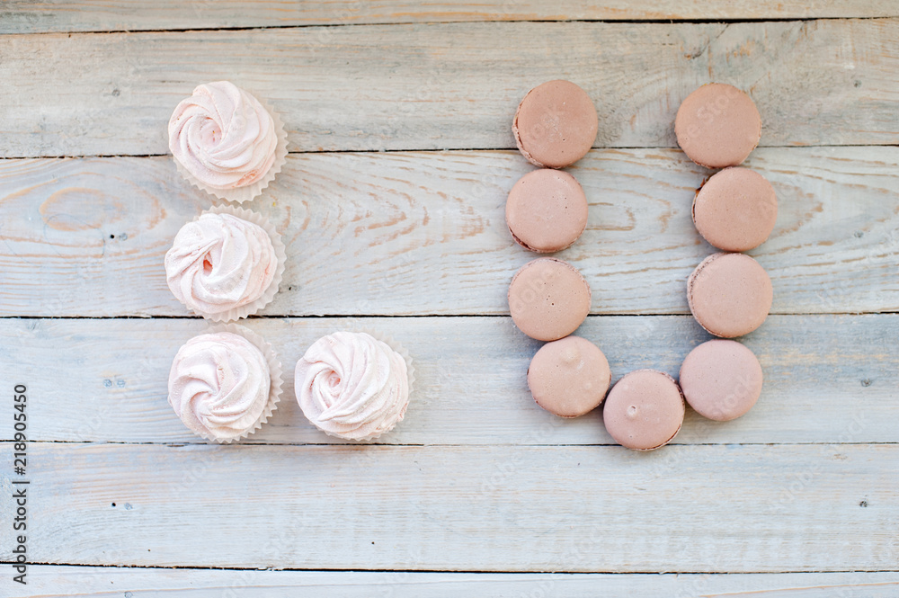 Tasty pink macaroons with cakes on a wooden table. It can be used as a background