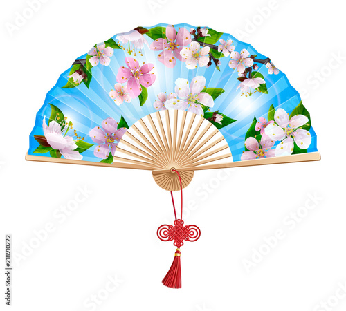 Chinese fan with a pattern of pink spring sakura flowers on blue sky. On the handle of the folding fan red wishful knot. Isolated on white background.