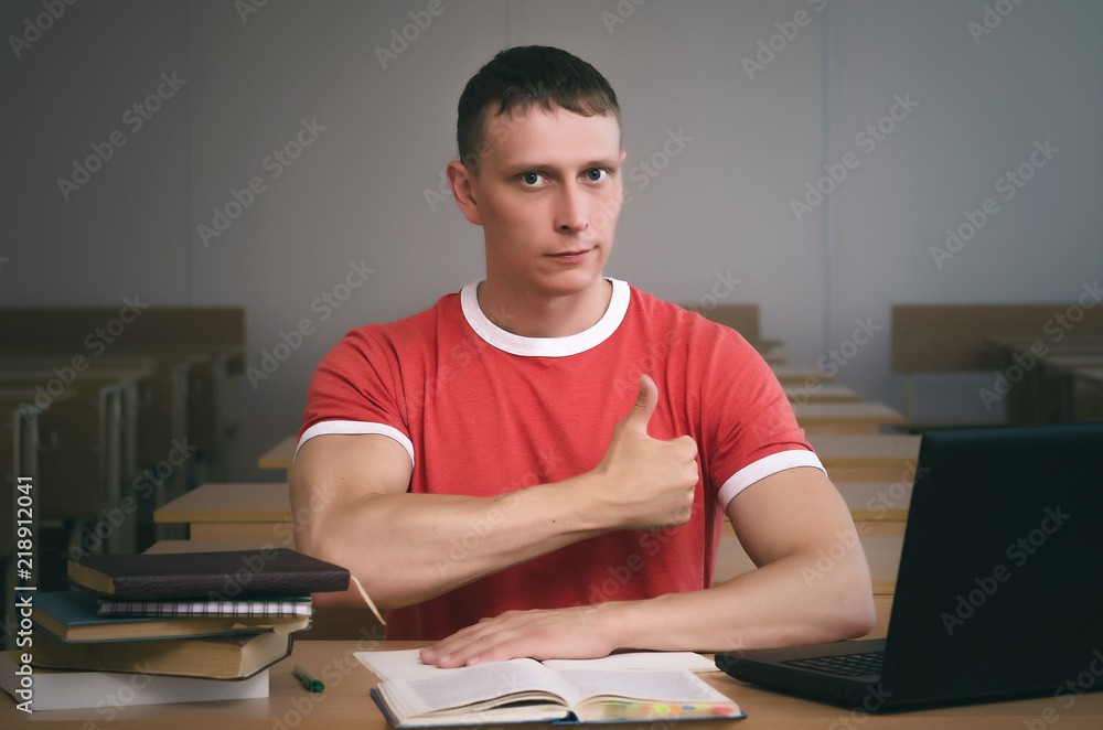 Young student boy sitting by the school desk and showing a thumbs up. Pass an exam concept. Young student boy sitting by the school desk and showing a thumbs up. Pass an exam concept.