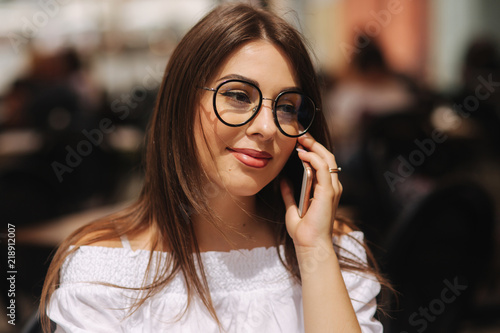 Portrait of outgoing lady telling by phone and waiting waiter. She looking at the street. Business and rest concept