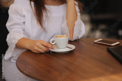 Close up fashion image of woman holding white cup of her morning cappuccino, wearing white stylish clothes and vintage sunglasses. Enjoy her time alone. Instagram colors