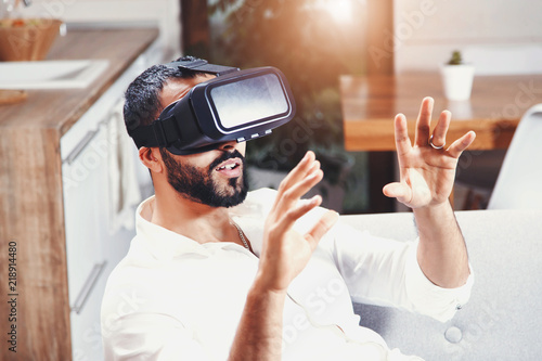 Happy multicultural bearded man getting experience using VR-headset glasses of virtual reality at home