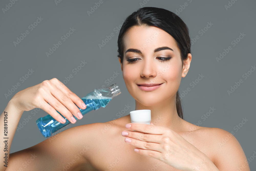 portrait of smiling woman with bare shoulders holding mouthwash isolated on grey portrait of smiling woman with bare shoulders holding mouthwash isolated on grey