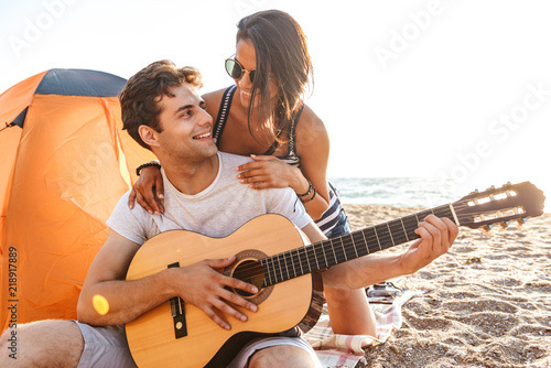 Young cute loving couple play guitar on the beach outdoors.