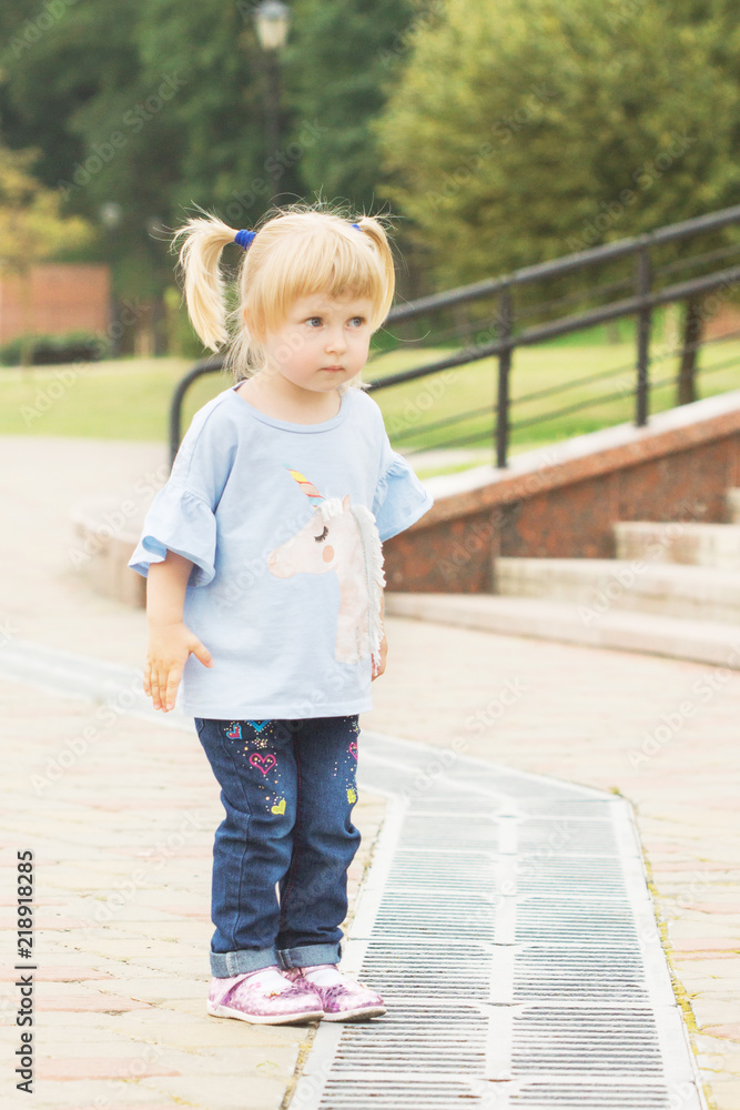 cheerful little blonde with two tails walking along the alley in the city park in summer sunny weather cheerful little blonde with two tails walking along the alley in the city park in summer sunny weather