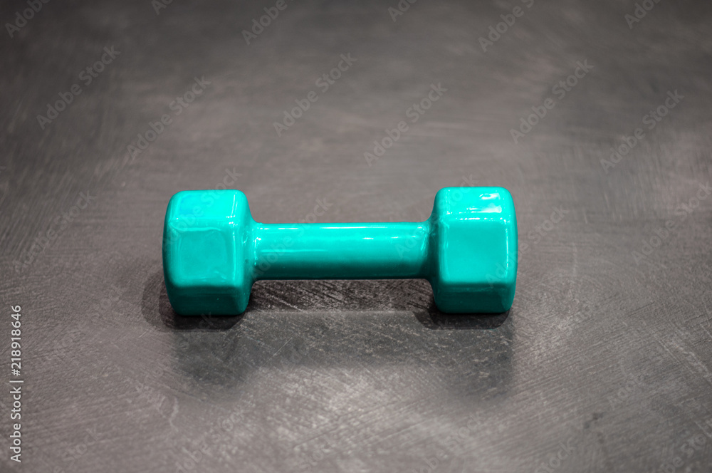 Dumbbell in a silicone shell of turquoise color on the gray floor Dumbbell in a silicone shell of turquoise color on the gray floor