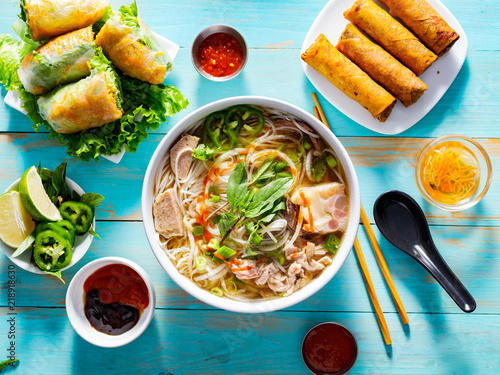 vietnamese pho bo soup with appetizers on table and drizzled with sriracha sauce