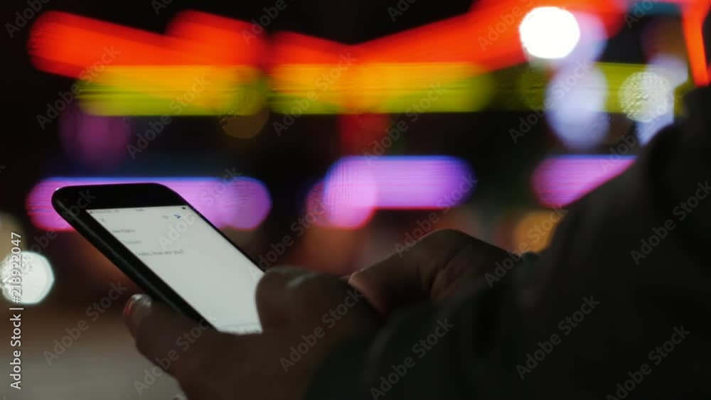 Typing message business mail on a smartphone device at night with urban cityscape defocused blurry bokeh background Typing message business mail on a smartphone device at night with urban cityscape defocused blurry bokeh background