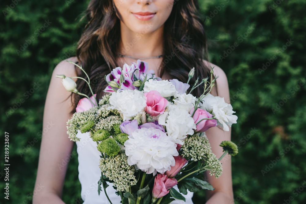 cropped view of beautiful woman posing in wedding dress and holding traditional bouquet cropped view of beautiful woman posing in wedding dress and holding traditional bouquet