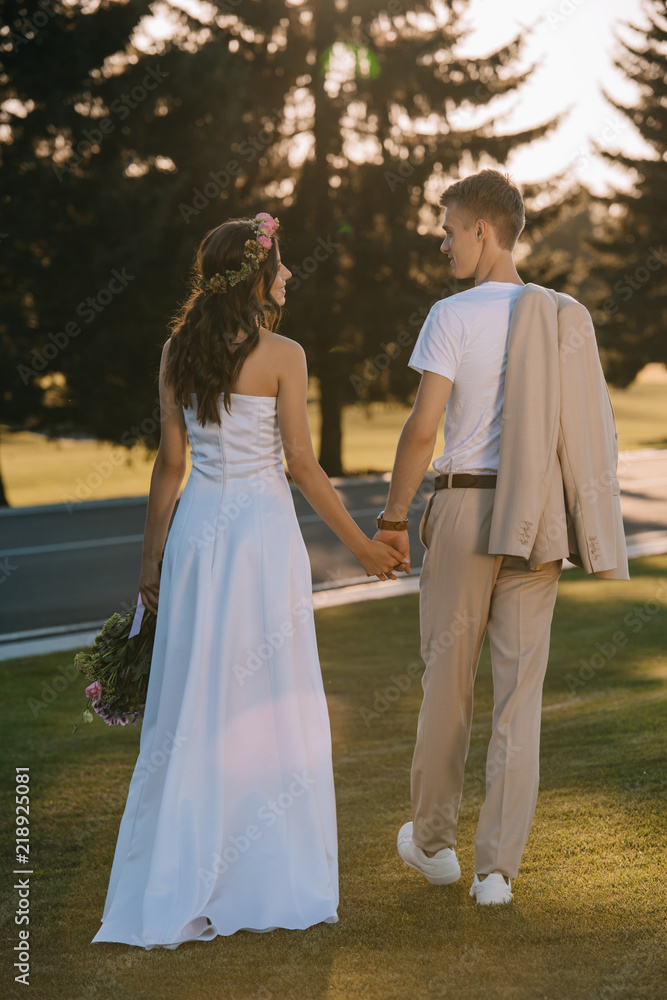 back view of attractive bride and handsome groom holding hands outdoors back view of attractive bride and handsome groom holding hands outdoors