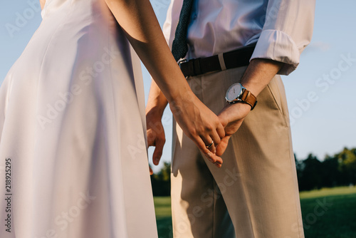 cropped shot of romantic young wedding couple holding hands in park
