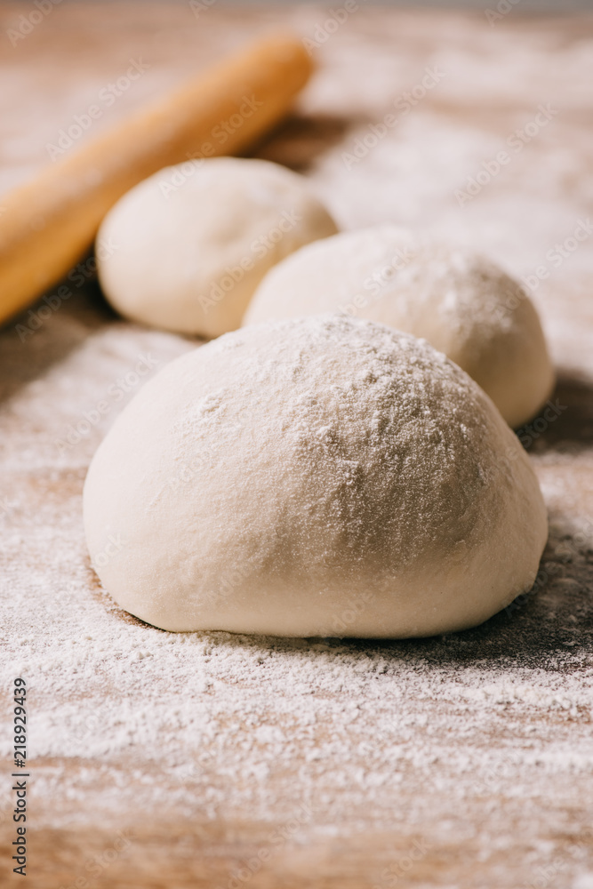 selective focus of raw dough for pizza and rolling pin on tabletop