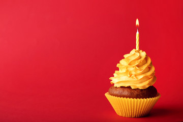 Tasty cupcake with candle on red background