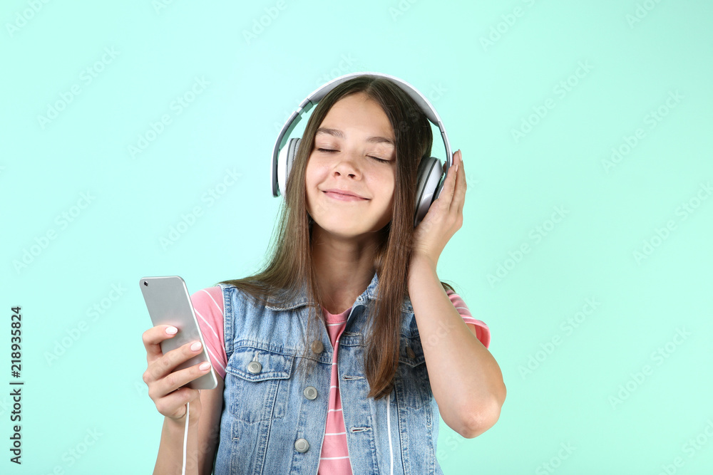 Young girl with headphones and smartphone on mint background Young girl with headphones and smartphone on mint background