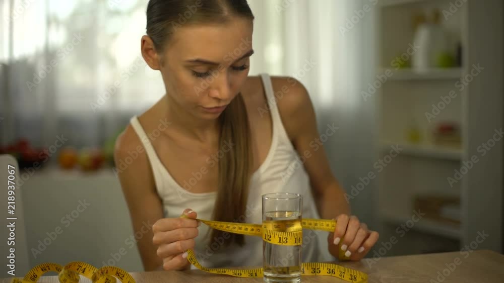 Anorexic girl measuring glass of water with tape, exhausted body, obsession Anorexic girl measuring glass of water with tape, exhausted body, obsession