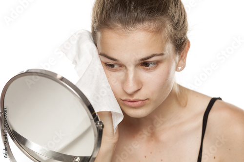 Young woman cleaning her face with wet wipe on white background
