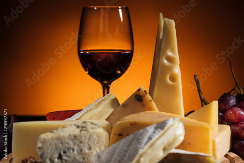 different types of appetizing cheeses and glass of wine on orange