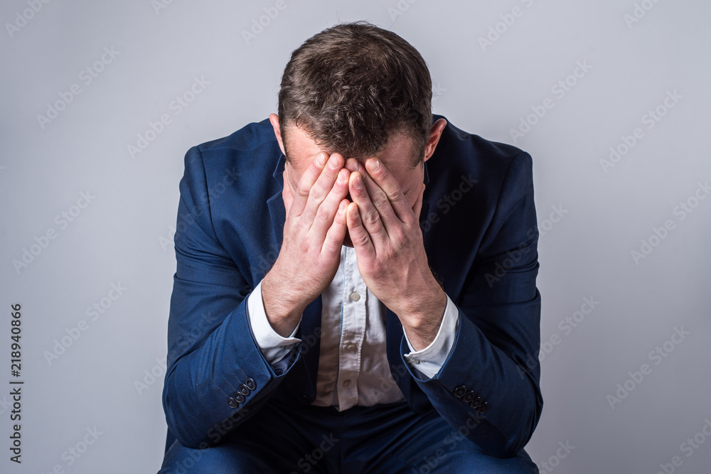 Portrait of a young handsome man in a suit, upset, hands on head, against plain studio background Portrait of a young handsome man in a suit, upset, hands on head, against plain studio background