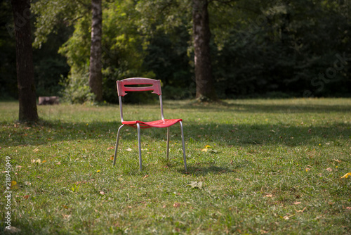 Old red chair in park on a green grass. Complementary colours.