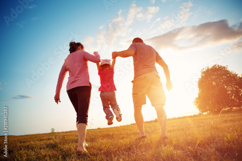 girl with mother and father holding hands on the nature. Child with parents outdoors photo