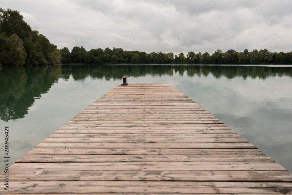 Old wooden dock, pier in to the lake with green water and green forest around the lake. Overcast day.