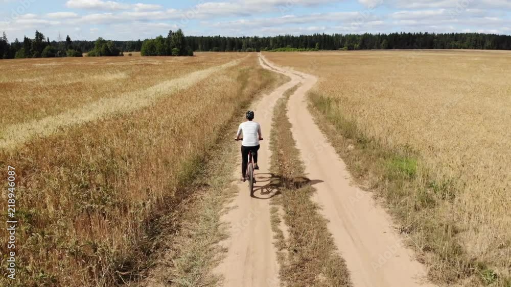 A young woman is riding a bicycle on the road through a field. View from above. Aerial photography A young woman is riding a bicycle on the road through a field. View from above. Aerial photography