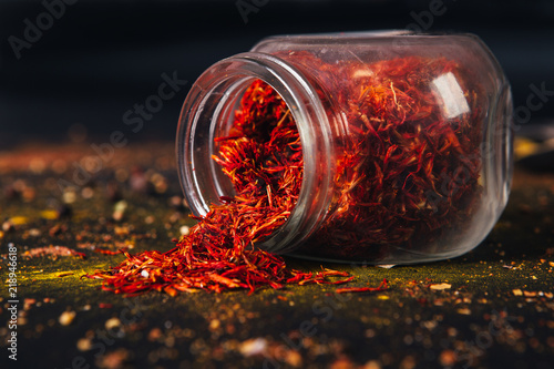 Saffron spice in an open glass jar on dark black background. Seasonings for food. Close-up.