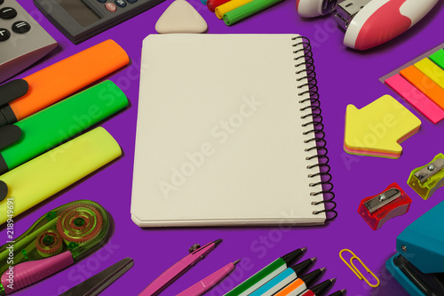 various stationary surrounding an opened notebook lying on a purple background. concept of office and educational chancery