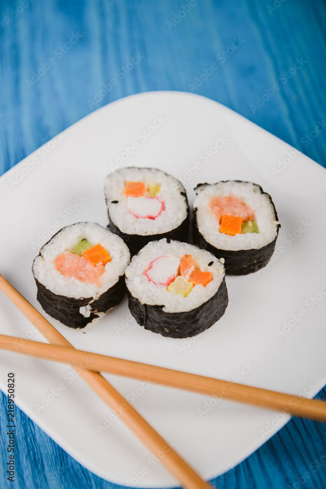 Delicious sushi rolls on white plate with two chopsticks. Blue wooden background. Delicious sushi rolls on white plate with two chopsticks. Blue wooden background.
