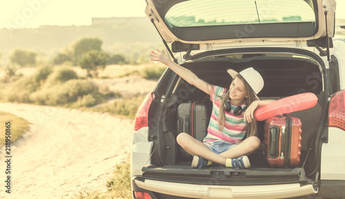Little cute girl in the trunk of a car with suitcases