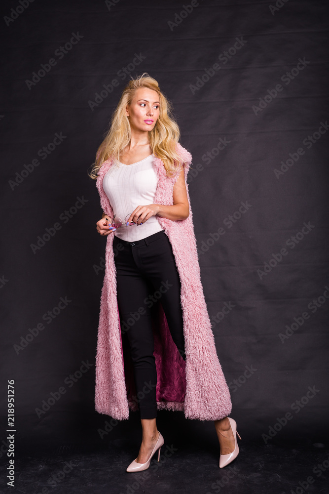 Fashion and beauty concept - blond model in pink cardigan posing over dark background Fashion and beauty concept - blond model in pink cardigan posing over dark background