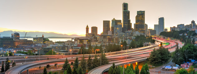 Panoramic view Seattle skylines and rush hour traffic on highway I-90 and I-5 interchange. Nearby density of homeless tents, tiny shelter in trees foreground on the left. Problem of urban life concept