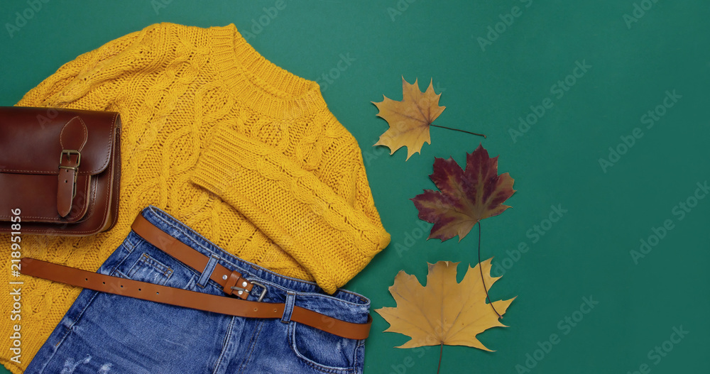 Φωτογραφία Female orange knitted sweater, blue jeans, leather bag and autumn leaves on green background top view flat lay
