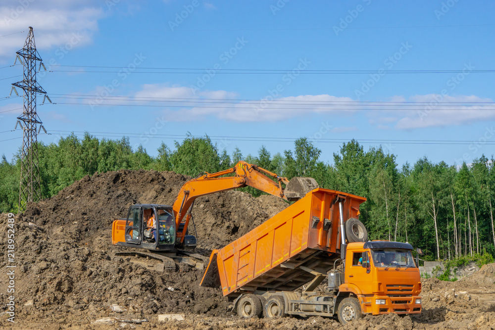 Orange excavator loads the soil in an orange truck Orange excavator loads the soil in an orange truck