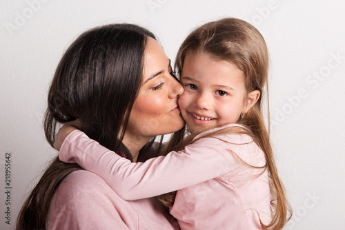 A close-up of a young mother kissing her small daughter in a studio.