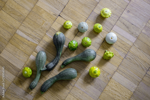 Four green zucchini with small scallop squashes over the light brown wooden background