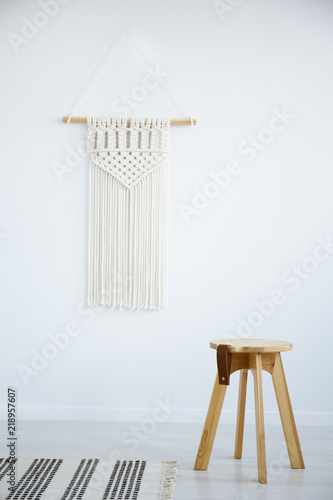 Wooden stool and rug in white simple living room interior with decor on the wall. Real photo photo