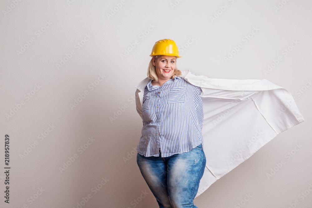 Portrait of an attractive overweight woman with yellow helmet and lab coat in a studio.