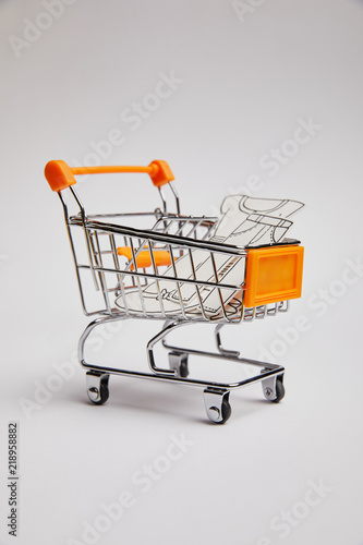 close up view of shopping cart with little clothes made of paper on grey background