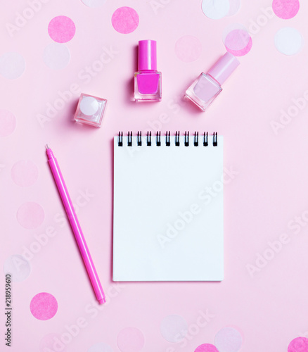 Empty note pad and colorful nail polishes on pink confetti background.